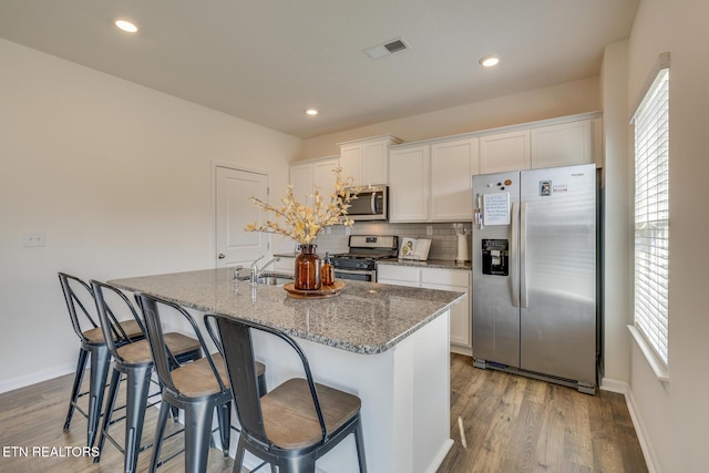 kitchen featuring white cabinetry, light stone counters, an island with sink, and appliances with stainless steel finishes