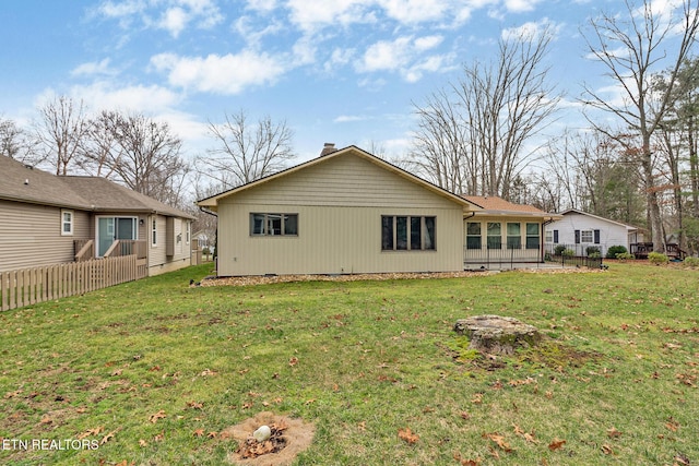 back of property with a chimney, fence, and a yard