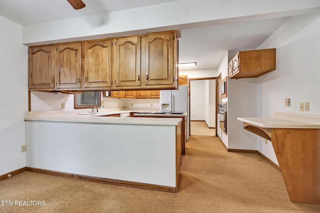 kitchen with baseboards, brown cabinetry, appliances with stainless steel finishes, a peninsula, and light countertops