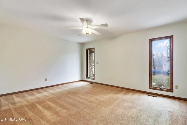 unfurnished room with a ceiling fan, light carpet, plenty of natural light, and baseboards