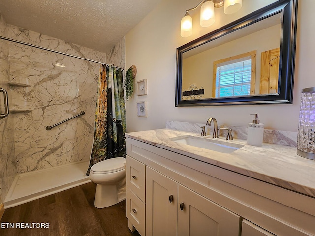 bathroom with toilet, vanity, a stall shower, wood finished floors, and a textured ceiling