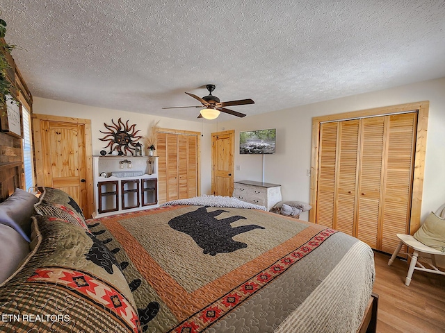 bedroom with two closets, wood finished floors, a ceiling fan, and a textured ceiling