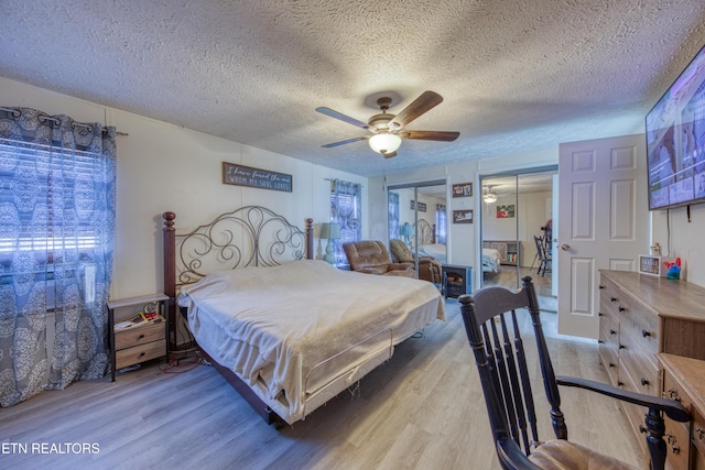 bedroom featuring hardwood / wood-style flooring, ceiling fan, multiple closets, and a textured ceiling