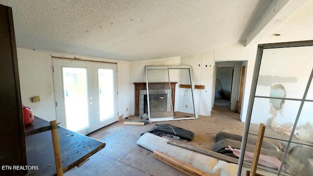 living room featuring vaulted ceiling, a tile fireplace, french doors, and a textured ceiling