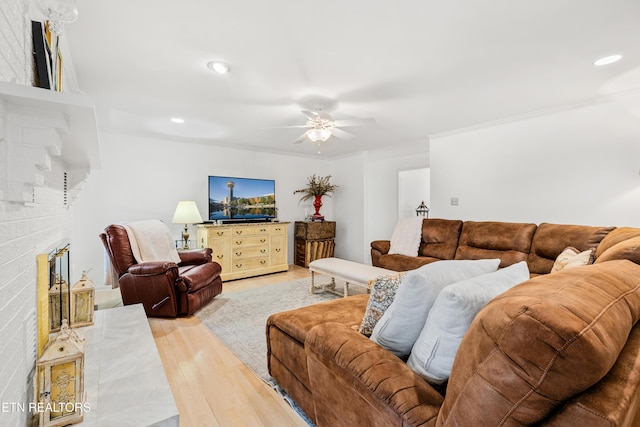 living room featuring light hardwood / wood-style flooring, ceiling fan, and a fireplace