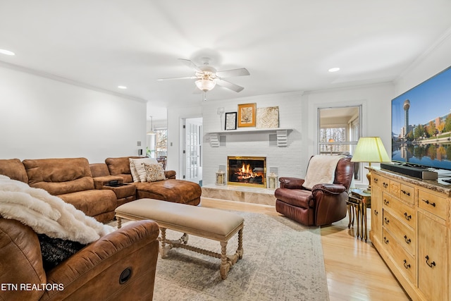 living room with a brick fireplace, ceiling fan, light hardwood / wood-style flooring, and crown molding