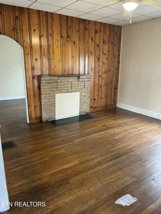 unfurnished living room with ceiling fan, dark hardwood / wood-style flooring, a drop ceiling, and wood walls