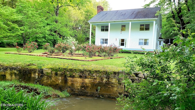 back of property with a chimney and a lawn