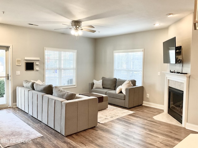 living area with visible vents, a ceiling fan, wood finished floors, a tile fireplace, and baseboards