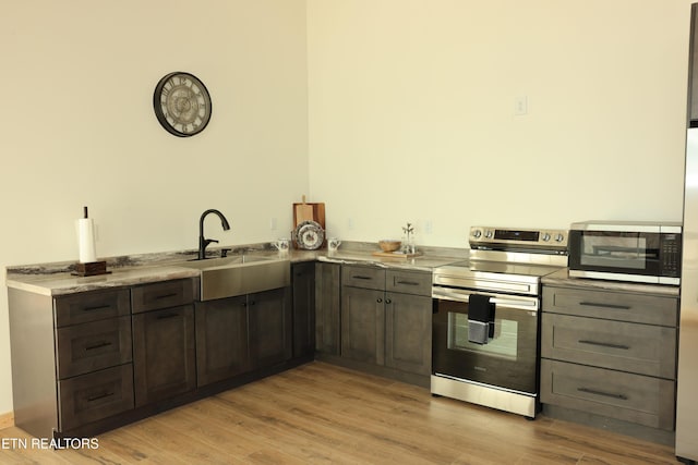 kitchen with stainless steel appliances, dark brown cabinets, sink, and light hardwood / wood-style floors