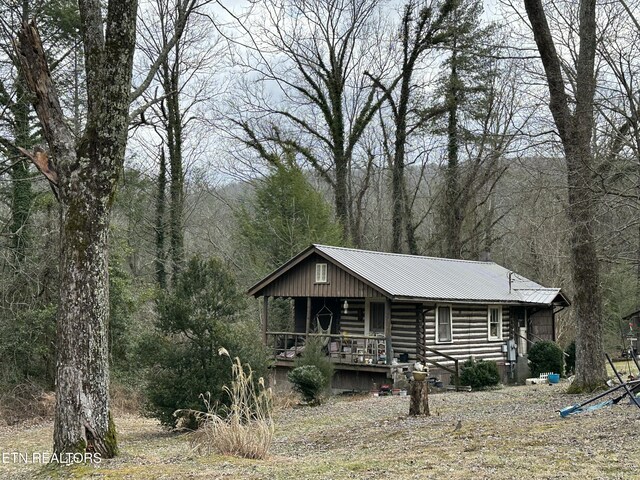 log cabin with a porch, metal roof, log exterior, and a wooded view