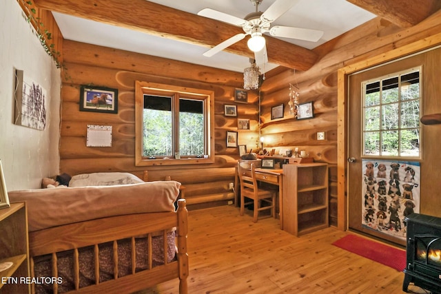 bedroom with a wood stove, hardwood / wood-style floors, and beam ceiling