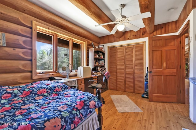 bedroom with ceiling fan, light wood-style floors, a closet, log walls, and beamed ceiling