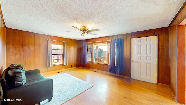 unfurnished living room featuring a textured ceiling, light hardwood / wood-style flooring, ceiling fan, and wood walls