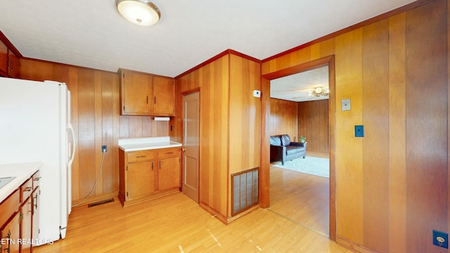 kitchen featuring crown molding, light wood-type flooring, wooden walls, and white refrigerator