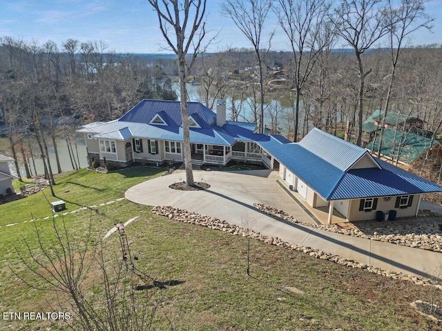 back of property with metal roof, a yard, concrete driveway, and a water view