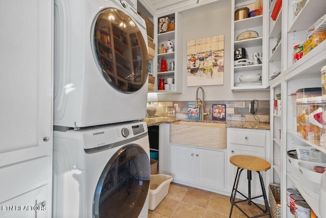 washroom with laundry area, light tile patterned flooring, a sink, and stacked washer and clothes dryer