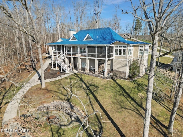 back of property featuring a chimney, a lawn, a sunroom, metal roof, and stairs