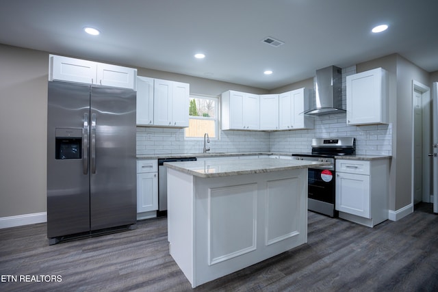 kitchen with wall chimney exhaust hood, appliances with stainless steel finishes, dark hardwood / wood-style floors, a kitchen island, and white cabinets