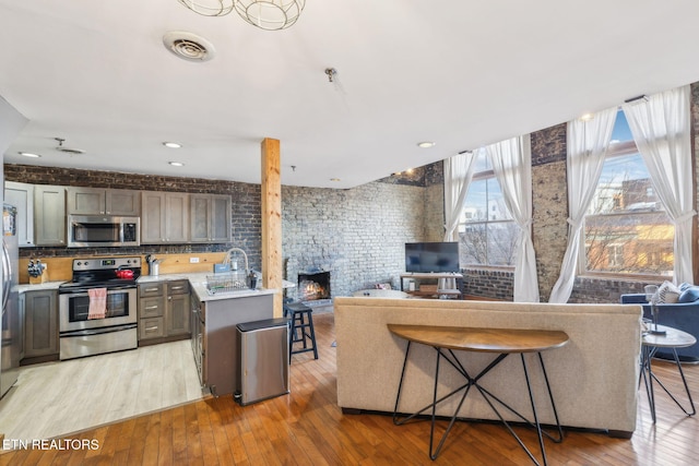 kitchen with stainless steel appliances, a stone fireplace, a kitchen breakfast bar, and light wood-type flooring