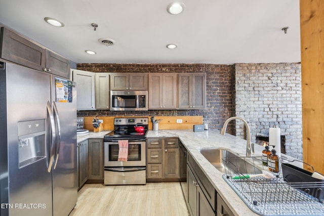 kitchen with appliances with stainless steel finishes, sink, decorative backsplash, light stone countertops, and light hardwood / wood-style flooring