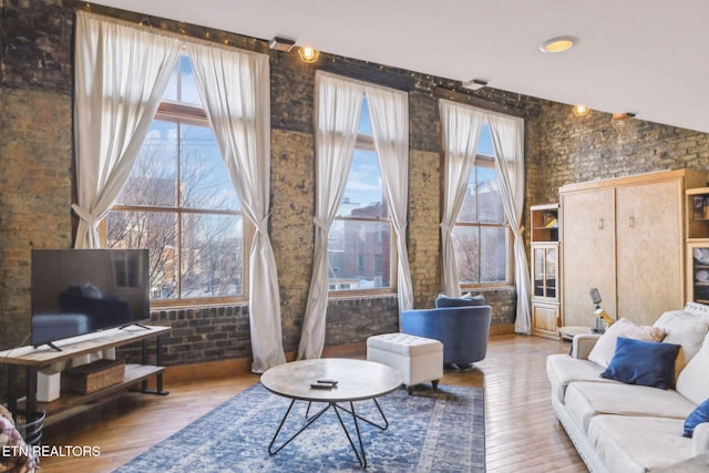 living room with hardwood / wood-style floors, a healthy amount of sunlight, and brick wall