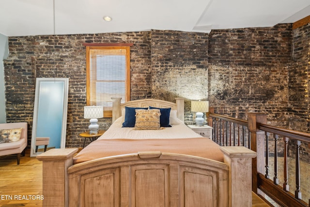 bedroom with brick wall and light hardwood / wood-style flooring