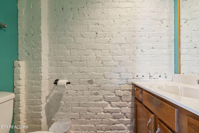 bathroom with vanity, toilet, and brick wall