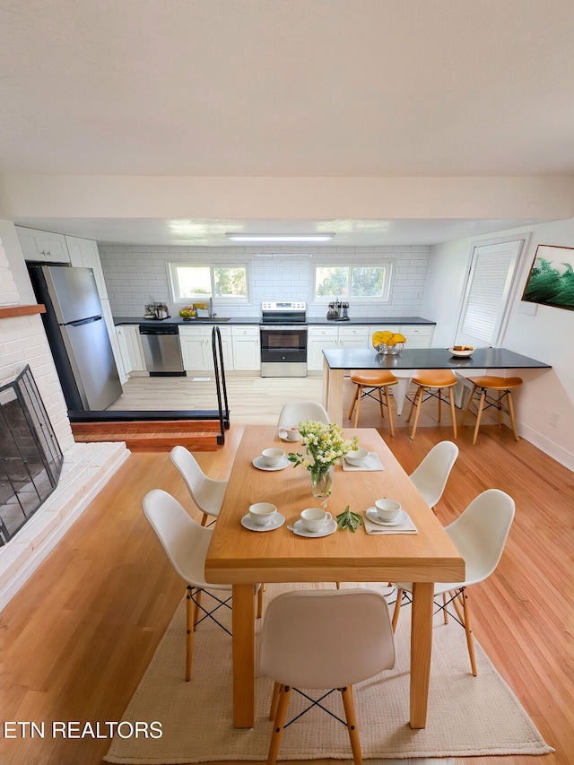 dining space with a brick fireplace, light wood-type flooring, and plenty of natural light