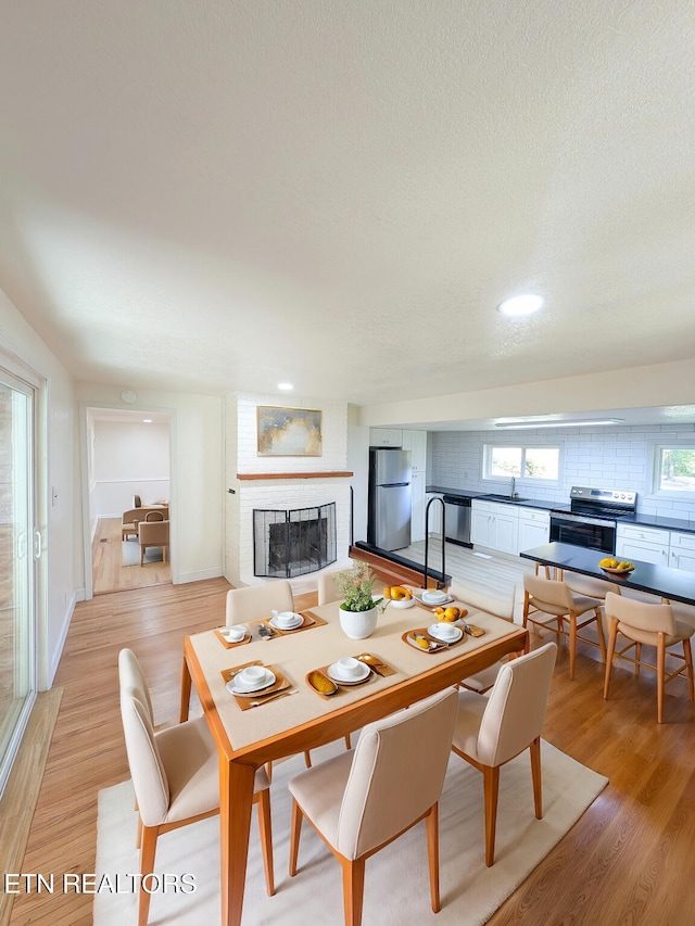 dining room with sink, light wood-type flooring, a brick fireplace, and a textured ceiling