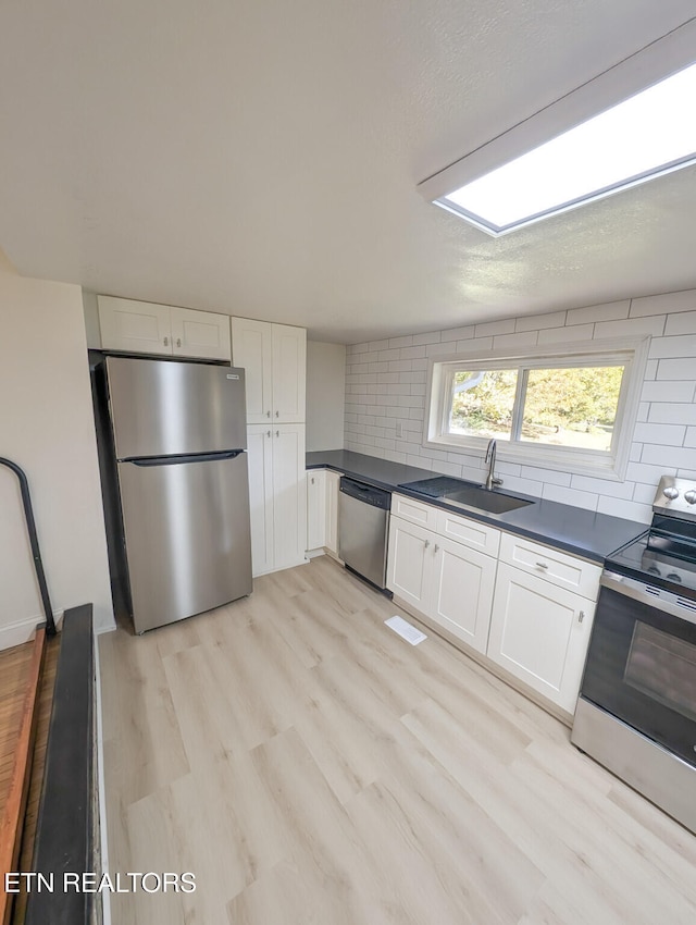 kitchen with white cabinetry, backsplash, appliances with stainless steel finishes, and light hardwood / wood-style flooring