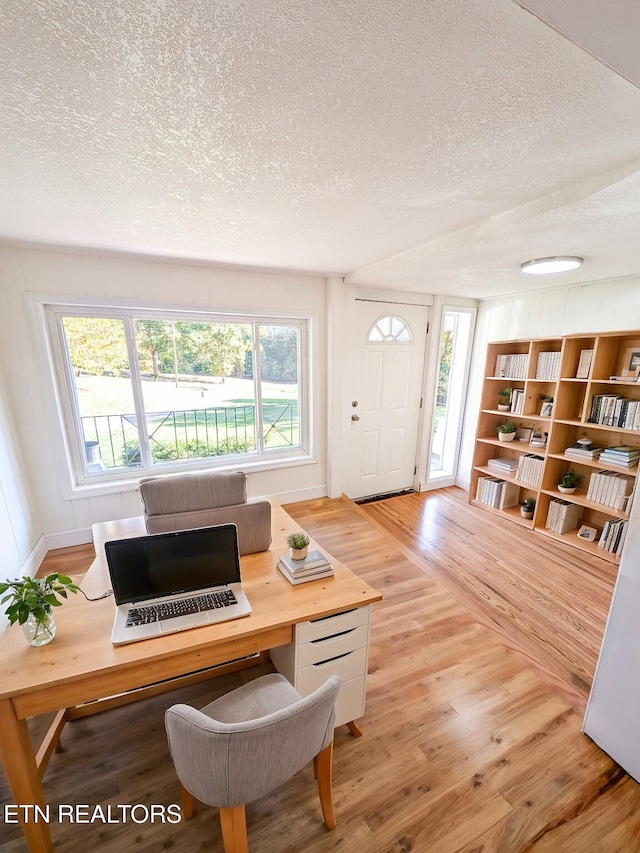 office area featuring built in shelves, wood-type flooring, and a textured ceiling