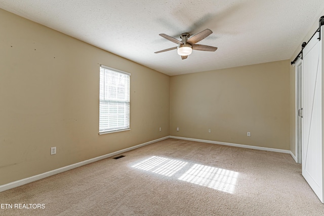 unfurnished bedroom with ceiling fan, light colored carpet, a barn door, and a textured ceiling