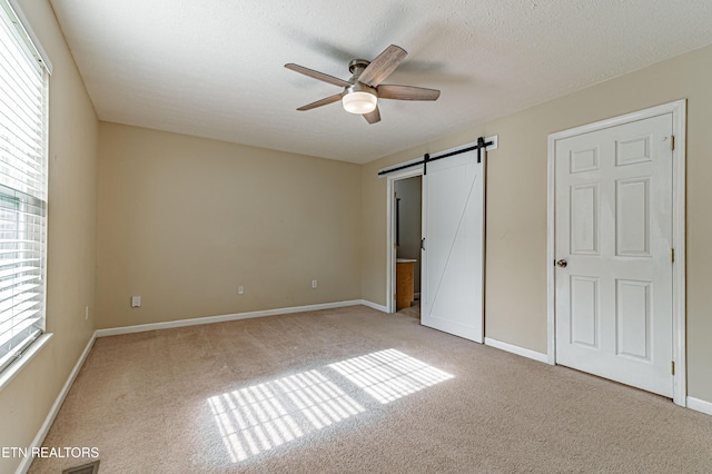 unfurnished bedroom with light carpet, ceiling fan, a barn door, and a textured ceiling