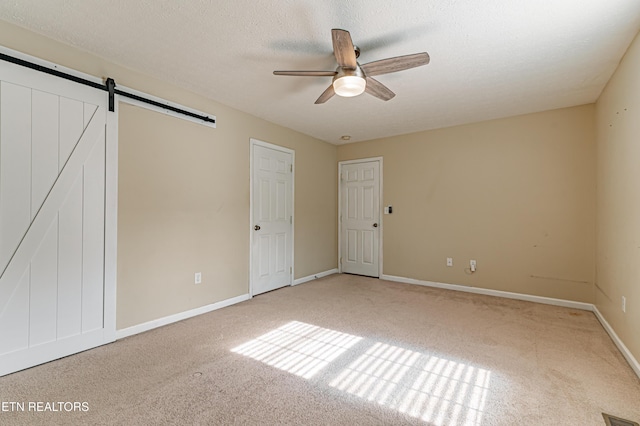 empty room with carpet flooring, ceiling fan, a barn door, and a textured ceiling