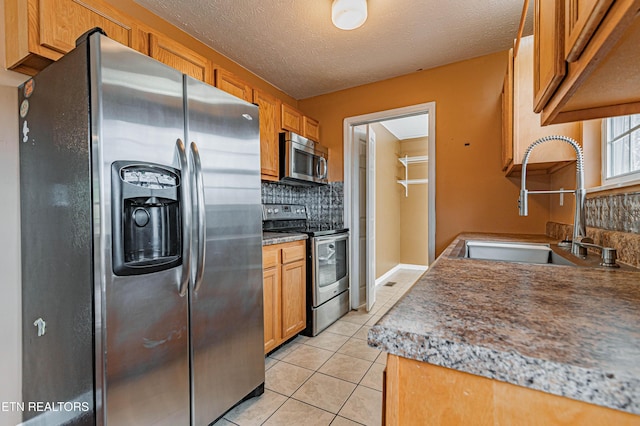 kitchen with light tile patterned floors, sink, appliances with stainless steel finishes, backsplash, and a textured ceiling