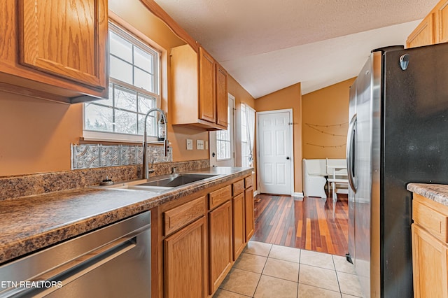 kitchen featuring lofted ceiling, sink, light tile patterned floors, stainless steel appliances, and a textured ceiling