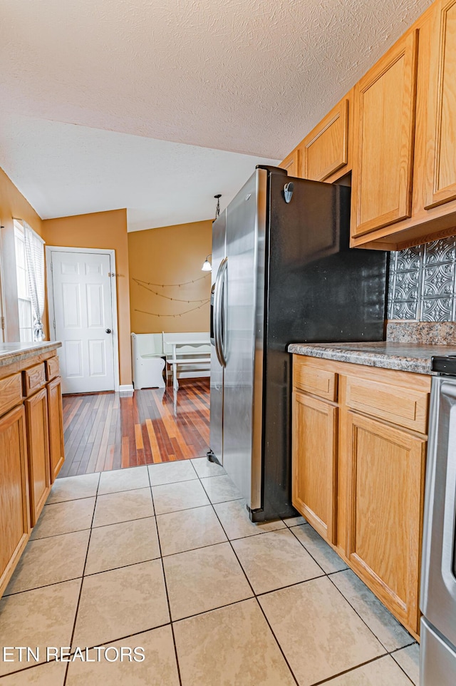 kitchen with stainless steel refrigerator with ice dispenser, lofted ceiling, range, a textured ceiling, and light tile patterned floors