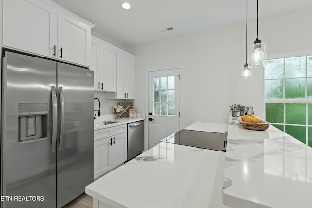 kitchen featuring stainless steel appliances, a sink, visible vents, white cabinetry, and decorative light fixtures