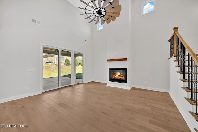 unfurnished living room with a wealth of natural light, a glass covered fireplace, baseboards, and wood finished floors