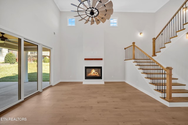 unfurnished living room with a glass covered fireplace, baseboards, a ceiling fan, and wood finished floors