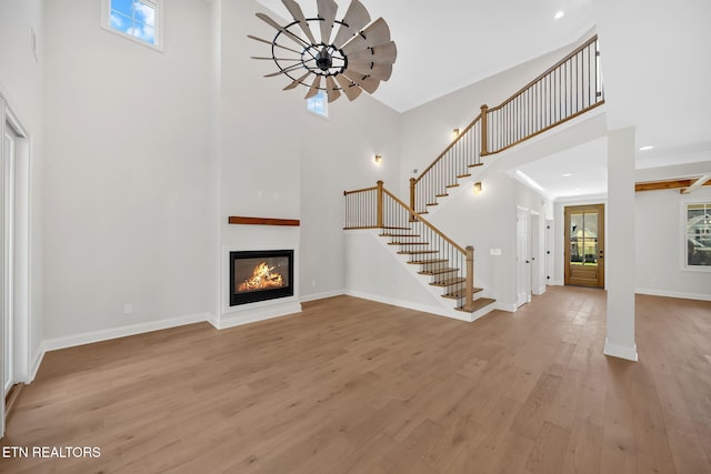 unfurnished living room with plenty of natural light, light wood-style flooring, stairs, and baseboards