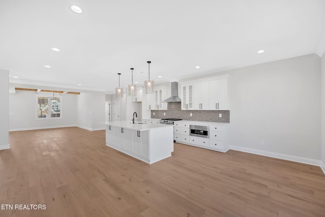 kitchen with built in microwave, a sink, white cabinetry, wall chimney range hood, and backsplash