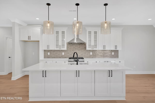 kitchen with light wood-type flooring, a kitchen island with sink, a sink, white cabinetry, and light countertops