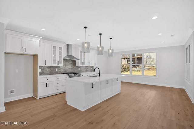 kitchen featuring a sink, light countertops, light wood-style floors, wall chimney exhaust hood, and backsplash