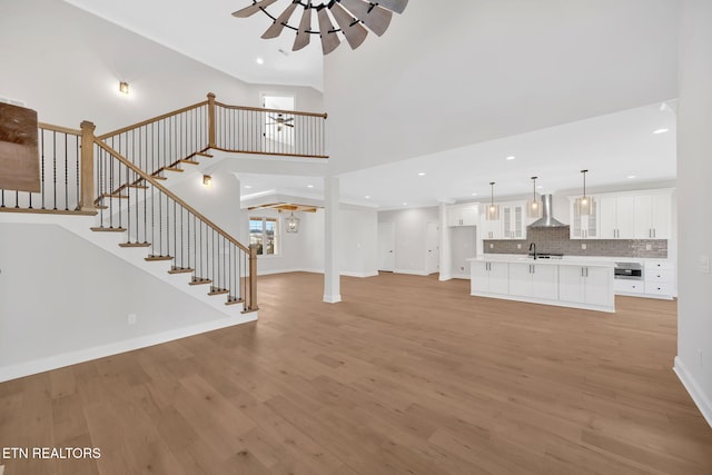 unfurnished living room with stairway, a ceiling fan, light wood-style floors, and a sink