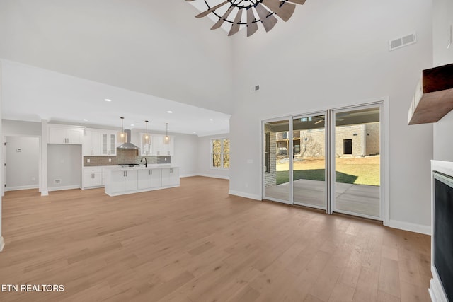 unfurnished living room with light wood finished floors, visible vents, a ceiling fan, and baseboards