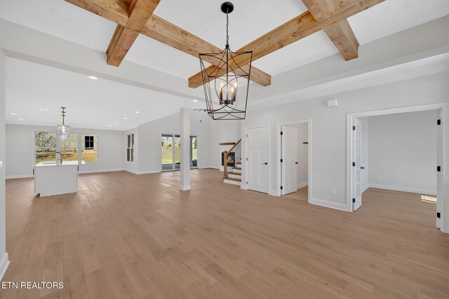 unfurnished living room featuring beamed ceiling, light wood finished floors, a chandelier, and stairway