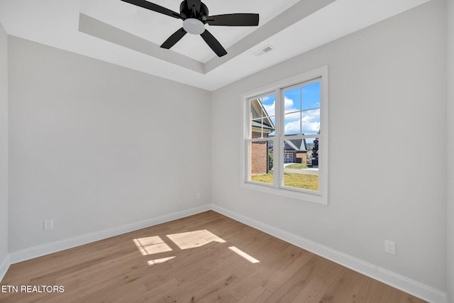 empty room featuring visible vents, a raised ceiling, baseboards, and wood finished floors