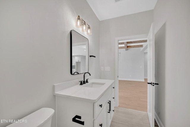 half bath with beamed ceiling, baseboards, toilet, and vanity